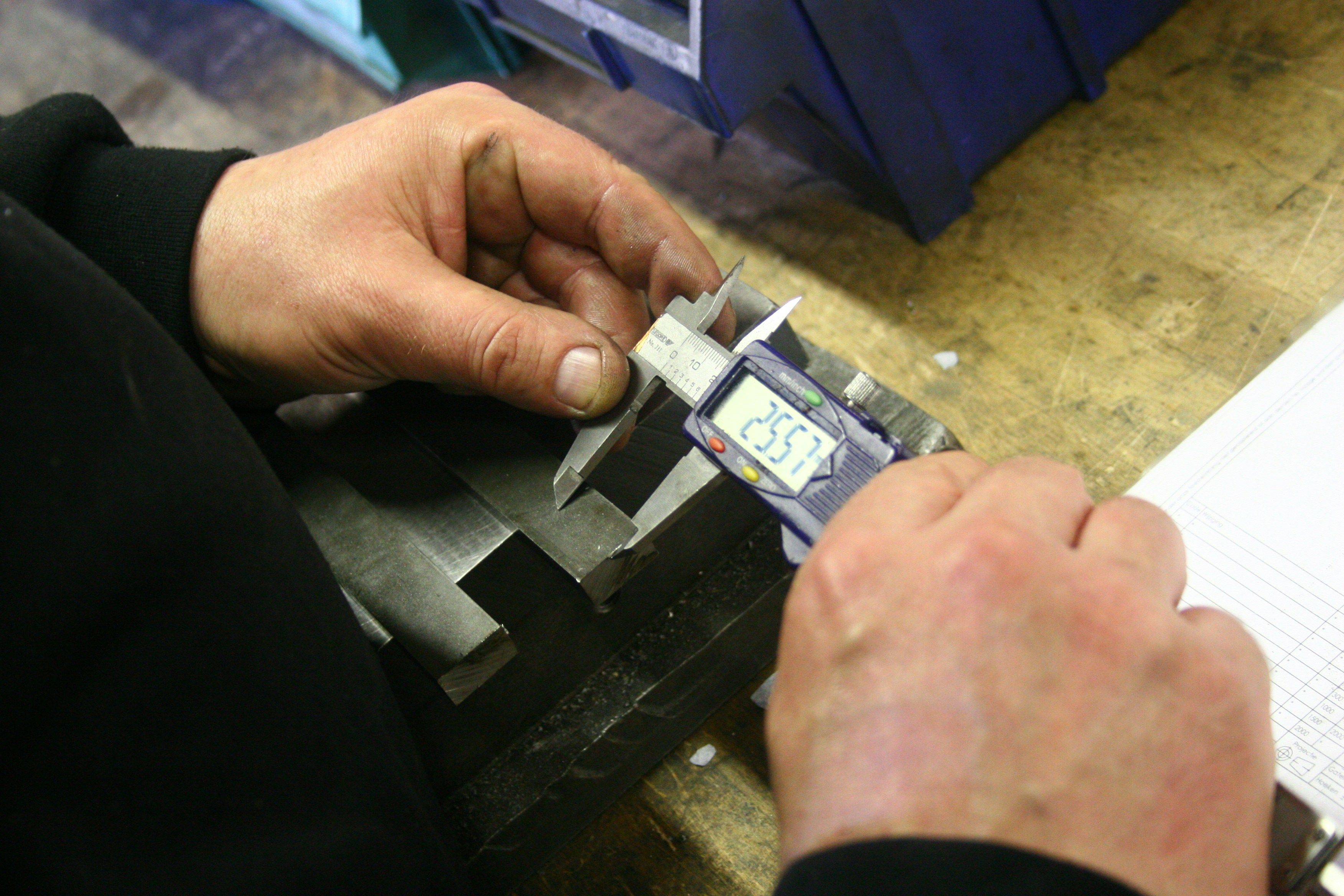Hands using a digital caliper to measure a metal part