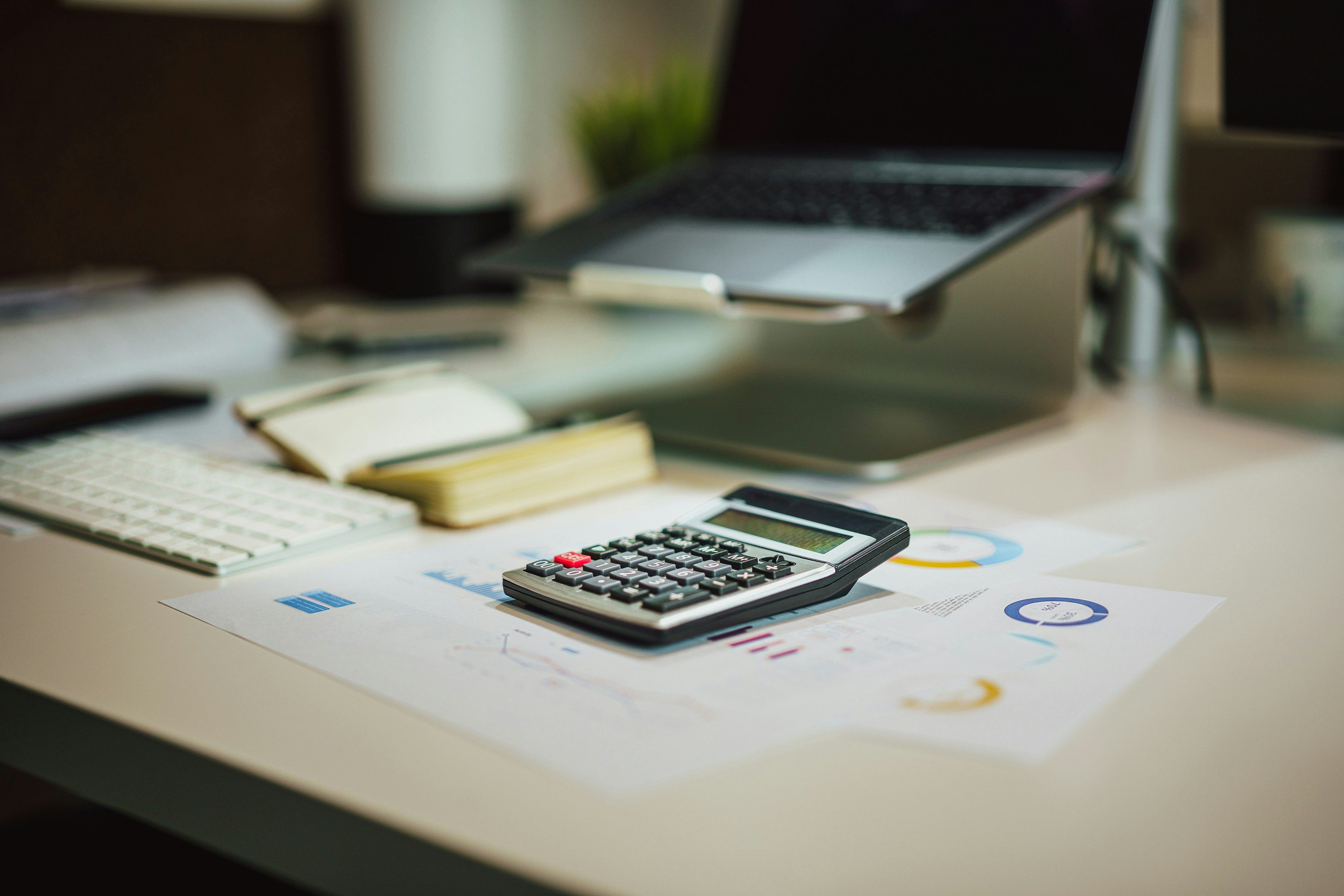 Calculator on printed charts at a desk, with a laptop and notebook behind it