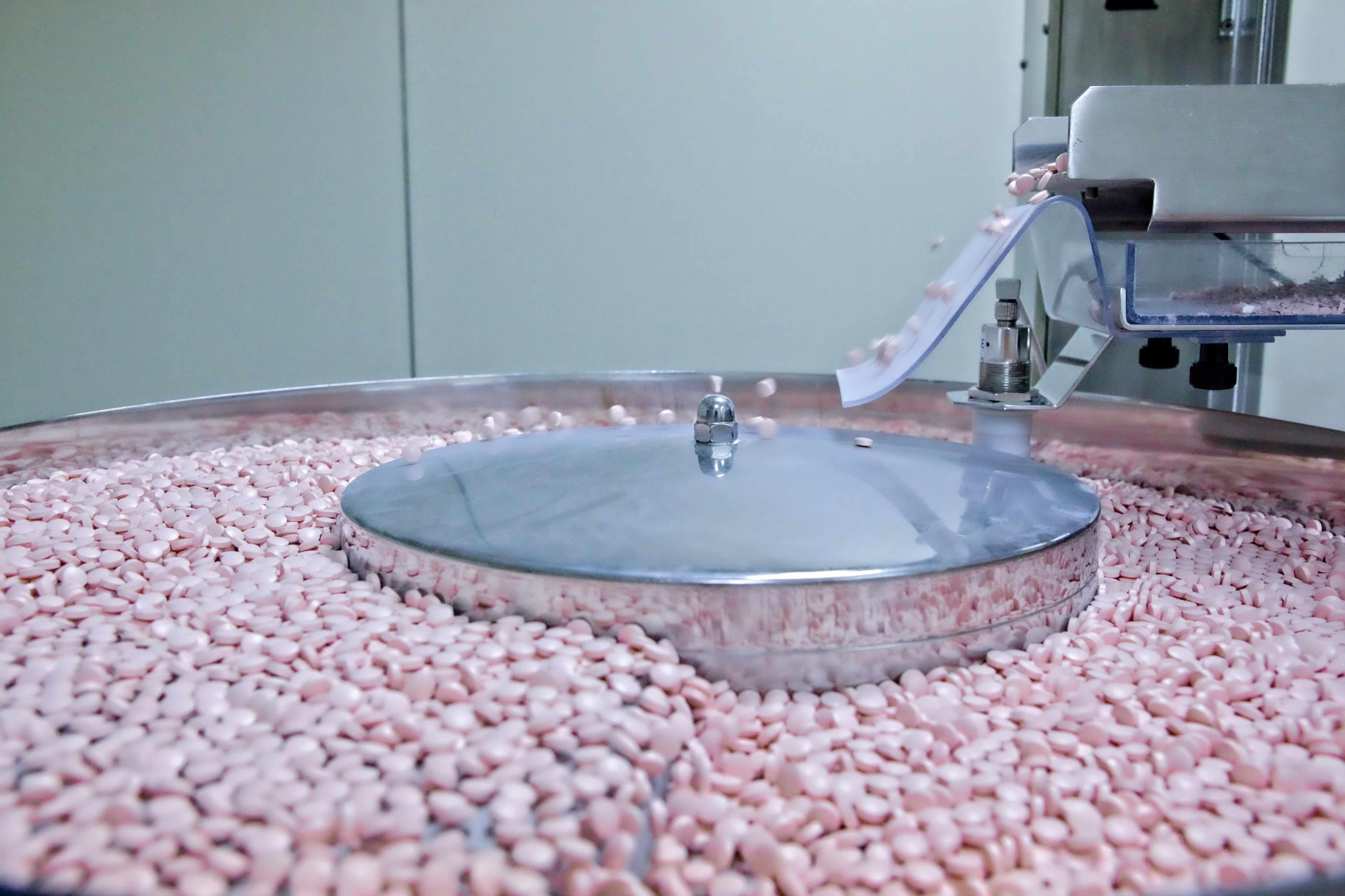 Small pink pills moving across a pharmaceutical production machine